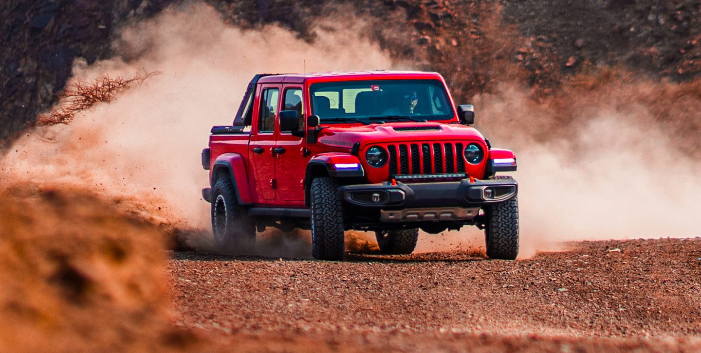 The 2022 Jeep Gladiator Mojave being driven off-road on sandy terrain with a large dust cloud obscuring its wheels.