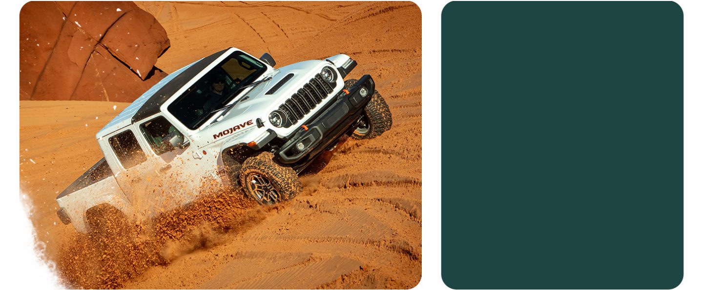 A white 2026 Jeep Gladiator Mojave X with its top removed, ascending a hill in the desert, kicking up sand as it goes.