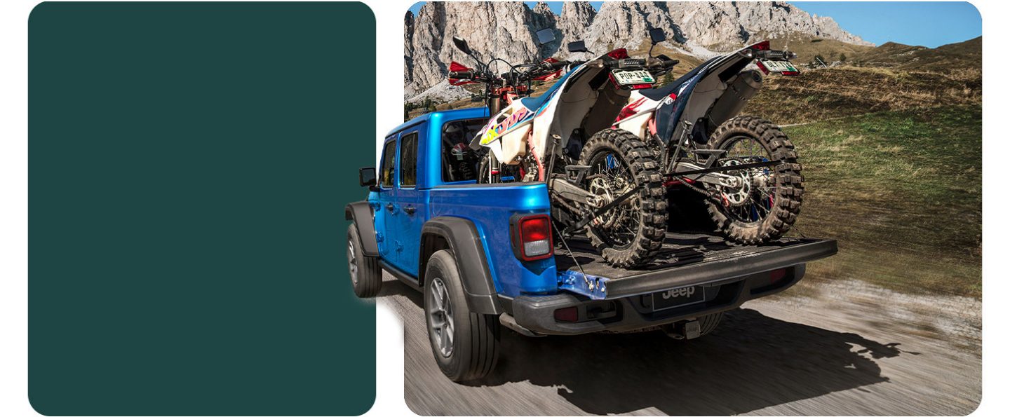 The rear of a blue 2026 Jeep Gladiator Sport S traveling on a trail off-road, with its tailgate open and two ATVs tied down in its pickup bed.
